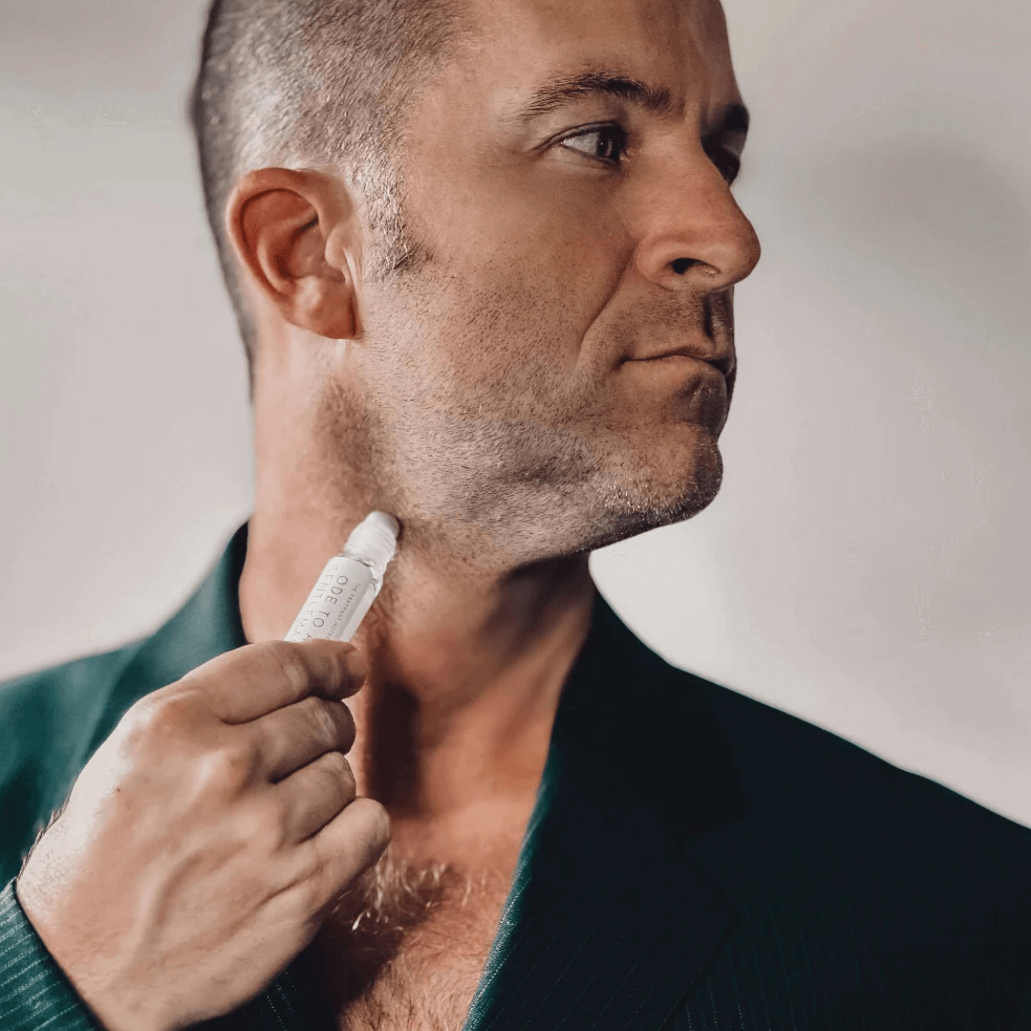 Man in black suit using Ode To a Gentleman Roll-On Fragrance on his neck.