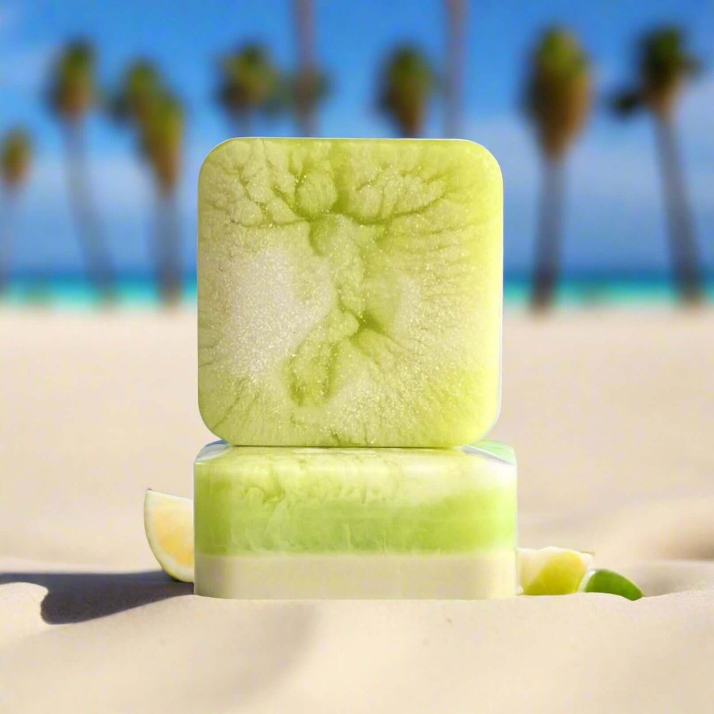 Two Sandy Keys soap bars sitting in the sand at the beach, with several pieces of lime next to the soap.